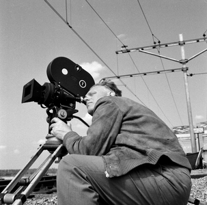 849526 Afbeelding van cineast Herman Wassenaar tijdens het filmen van treinen bij de spoorbrug over het ...